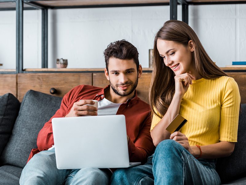 cheerful couple doing online shopping and smiling on sofa